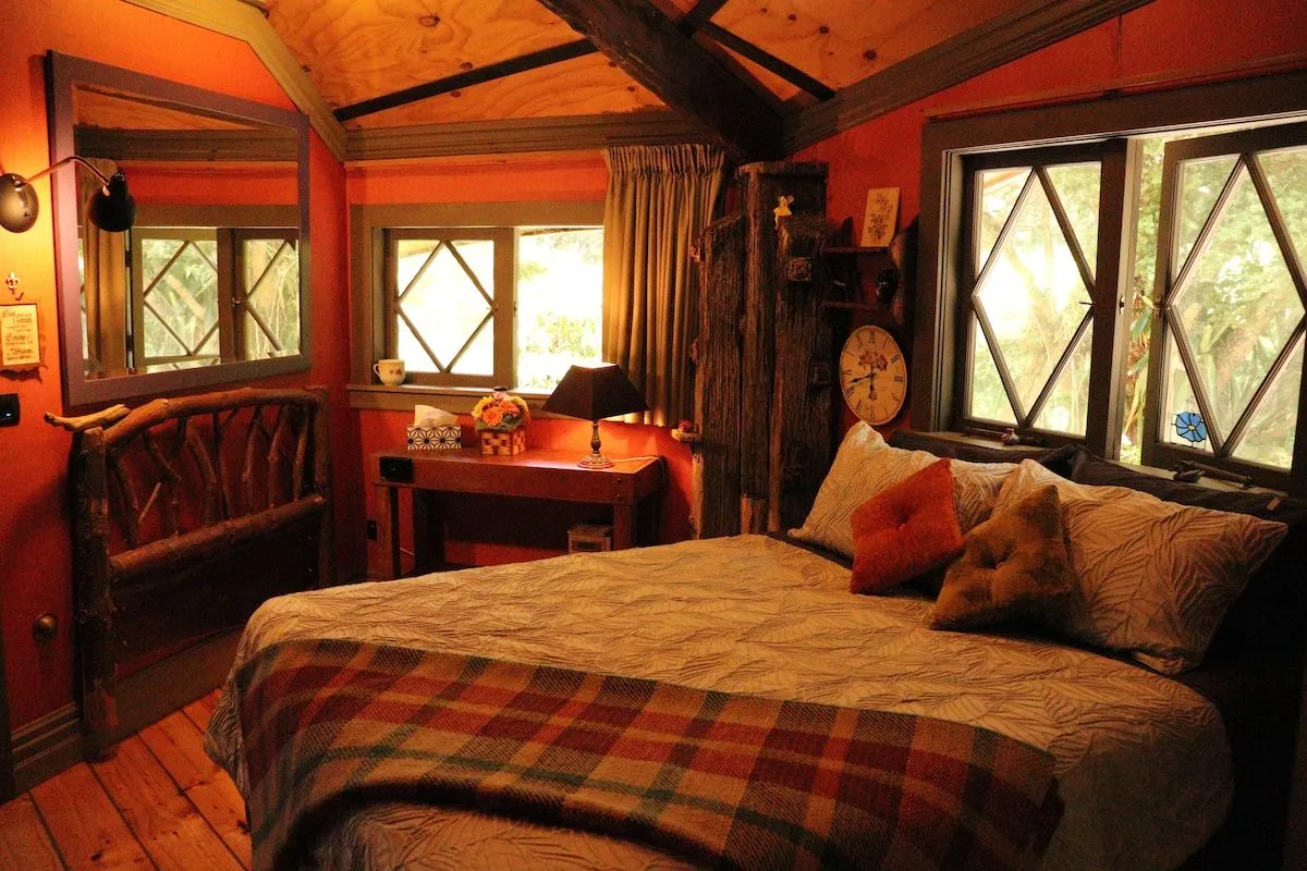 The bedroom, with a queen bed under diamond-lattice windows looking into the trees.