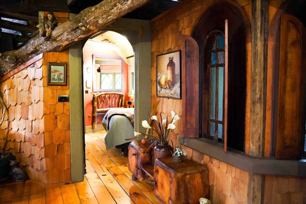 An interior hallway with shingled timber walls and an arched opening through to the bedroom.