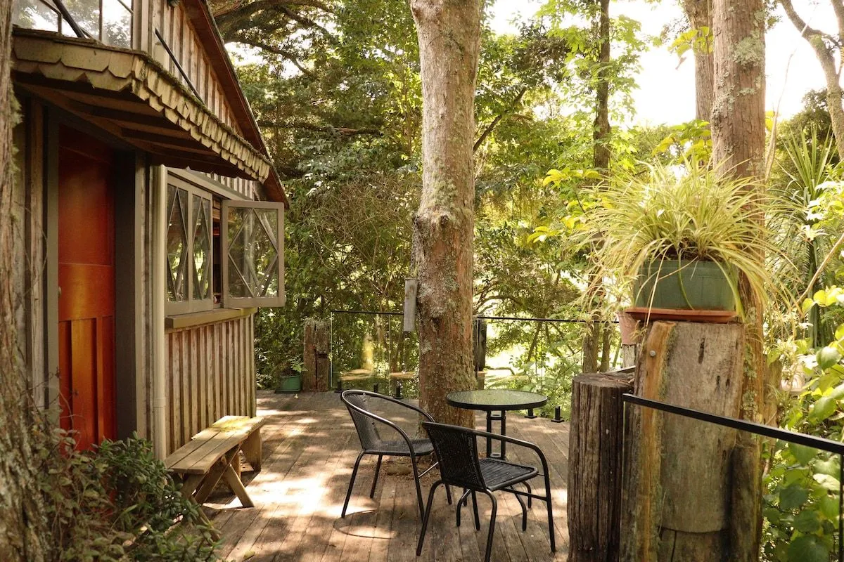 A table and chairs on the deck beside the treehouse, shaded by tall trees.