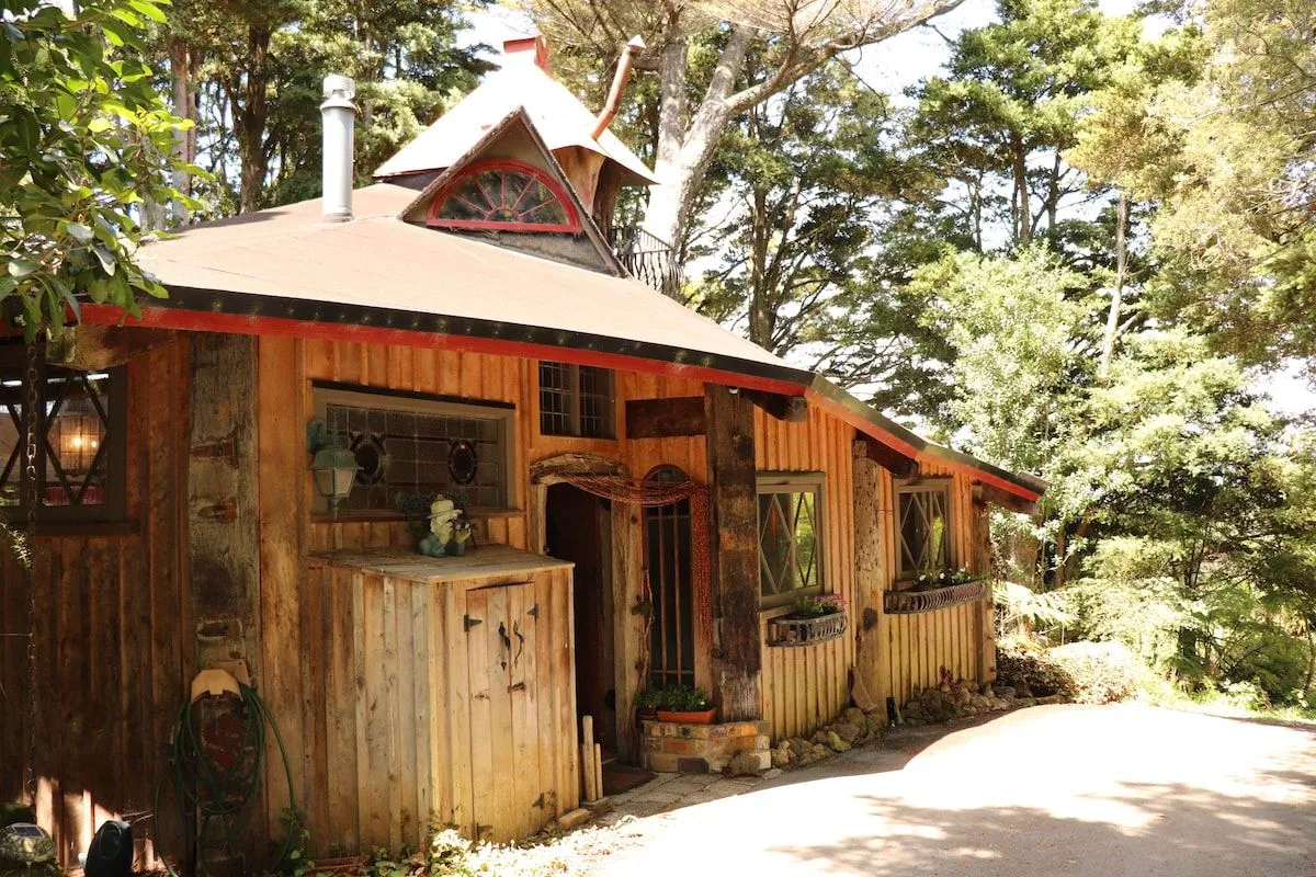 The timber treehouse from the driveway, with a shingled roof, stained-glass windows and a peaked turret.
